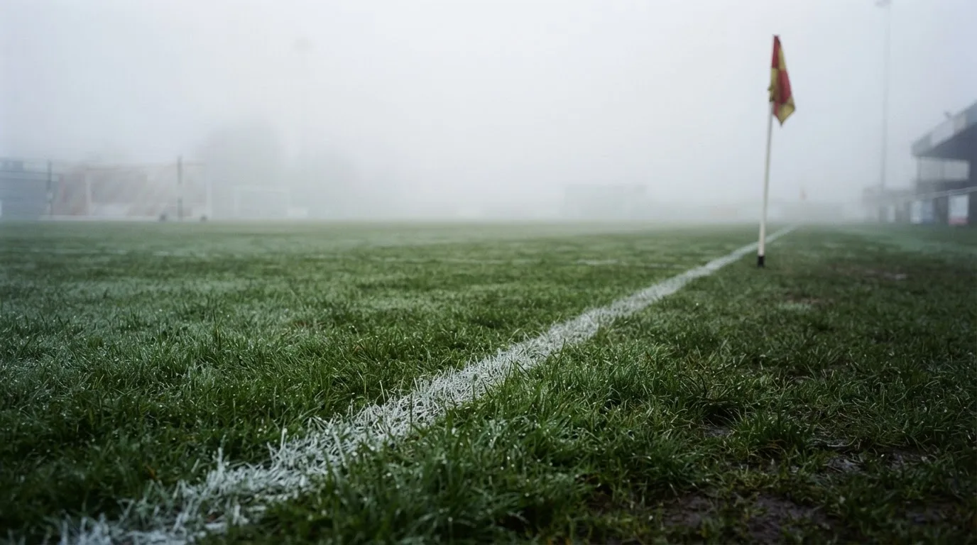 Der Rand eines Spielfelds mit weißer Linie und Eckfahne bei Nebel am frühen Morgen, ohne Menschen.
