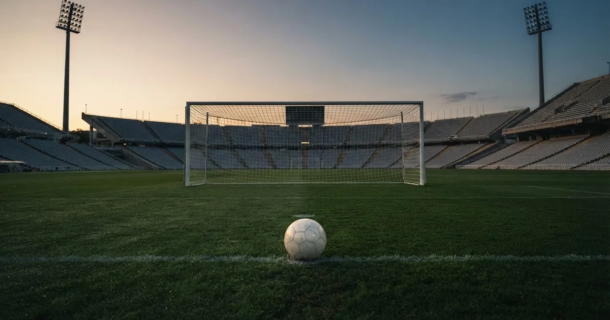 Ein Fußball liegt im Strafraum direkt vor dem Tor mit Netz, im Hintergrund leere Ränge bei Dämmerung.