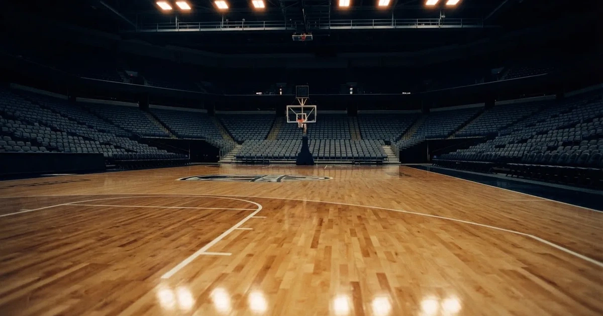 Eine leere Basketballhalle mit glänzendem Parkett und einem Korb im Hintergrund, Licht von Deckenstrahlern spiegelt sich im Boden.