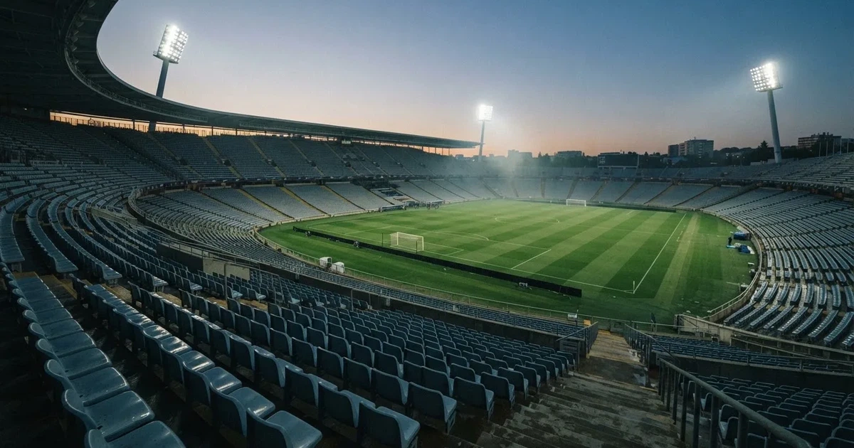 Leere Sitzreihen eines großen Stadions unter Flutlicht, dahinter die ferne Sicht auf den hell beleuchteten Rasen nach Sonnenuntergang.
