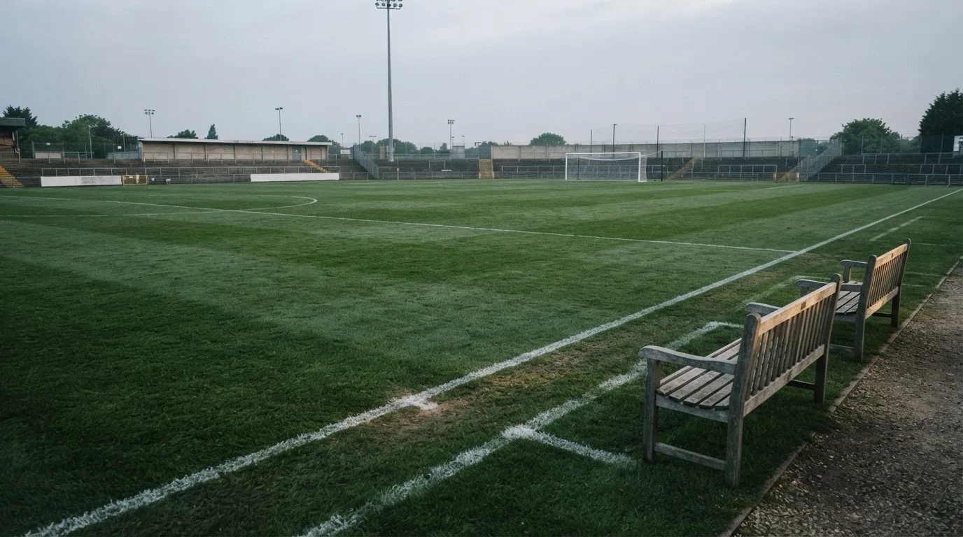 Ein Fußballplatz mit frisch gezogenen Kreidelinien im ersten Morgenlicht, leere Ersatzbänke am Spielfeldrand.