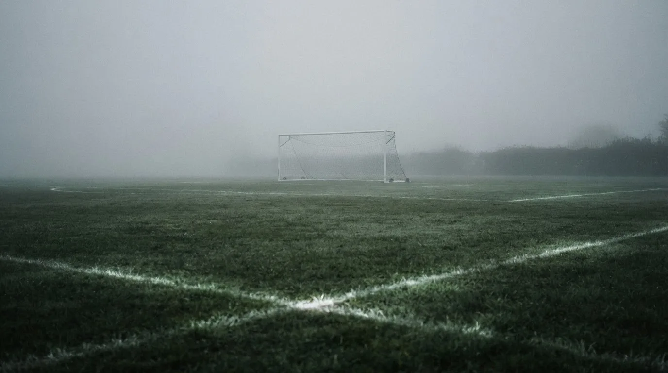 Ein Fußballtor mit Netz im Morgennebel auf einem leeren Platz, die Linien nur schwach zu erkennen.