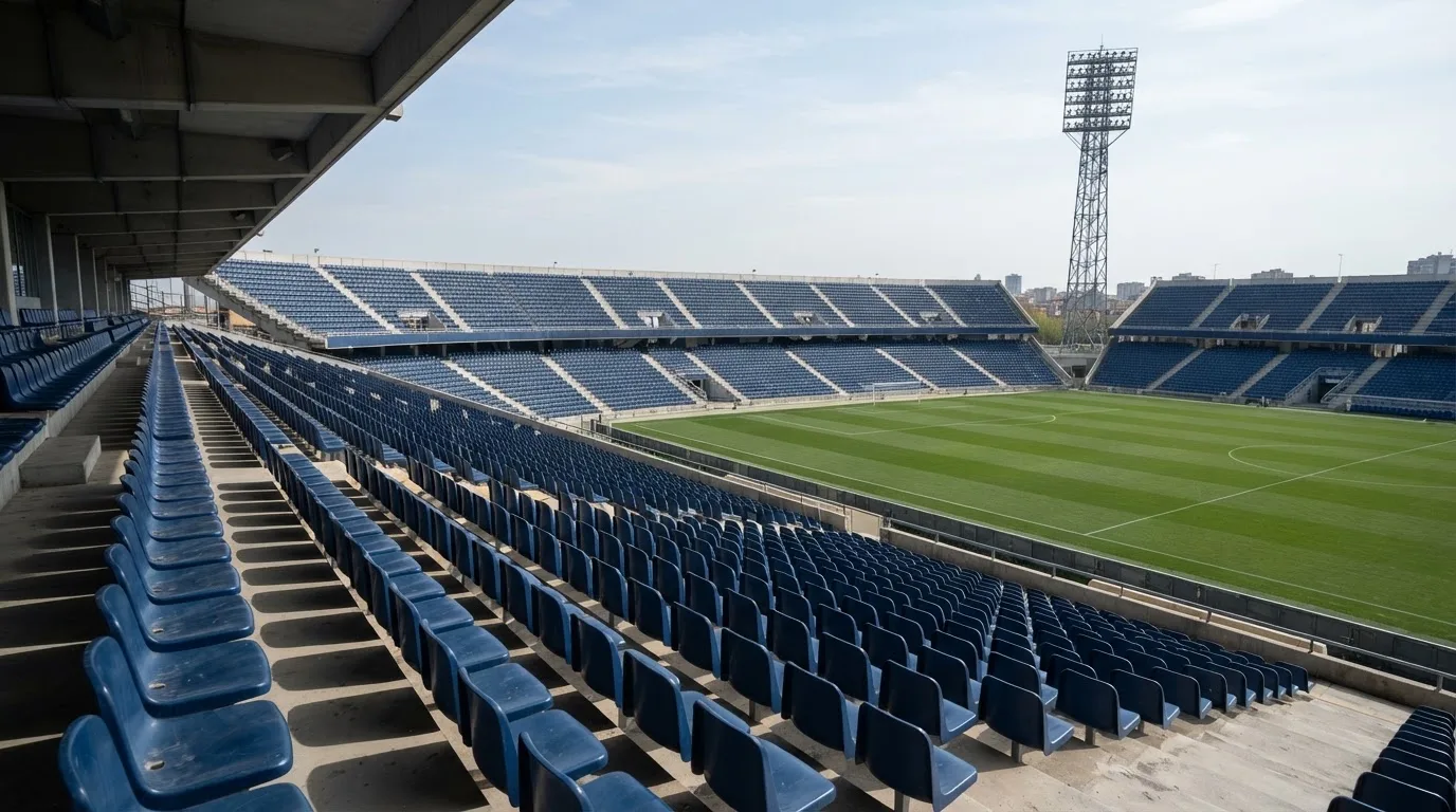 Eine leere Tribüne eines Fußballstadions bei Tageslicht, Sitzschalen in Reihen und dahinter ein Flutlichtmast.