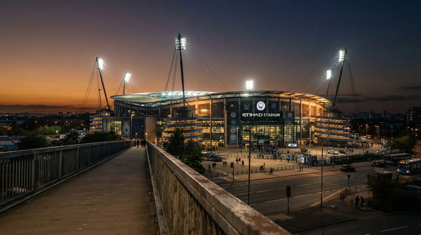 Ein Stadion bei Dämmerung mit eingeschalteten Flutlichtmasten, von einer Brücke aus aufgenommen.