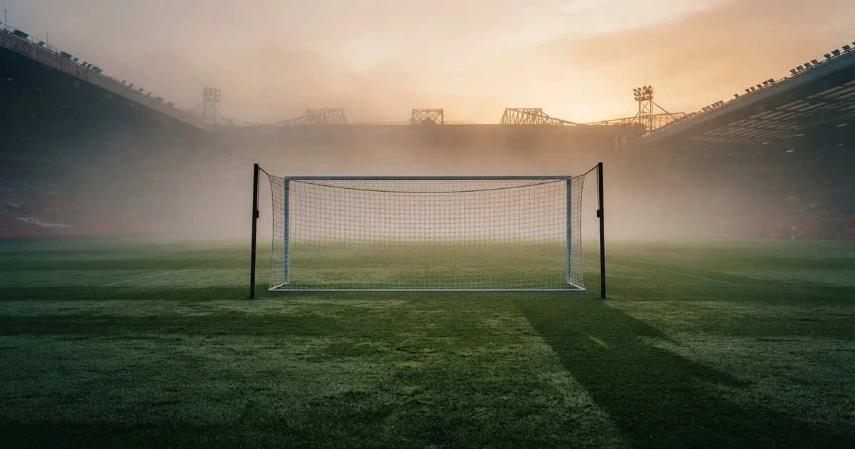 Ein Fußballtor mit Netz steht auf einem leeren Platz im Nebel der Morgendämmerung, der Rasen ist taufeucht.