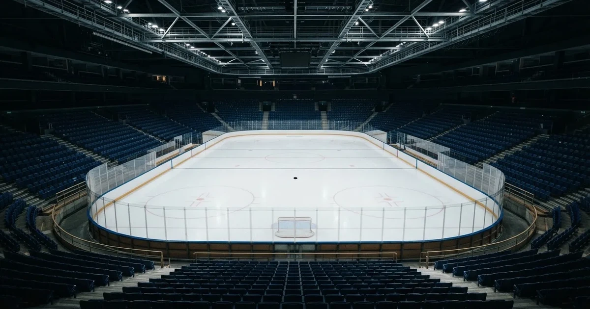 Eine leere Eisfläche in einer Halle mit Banden und Flutlicht, auf dem Eis liegt ein einzelner Puck.