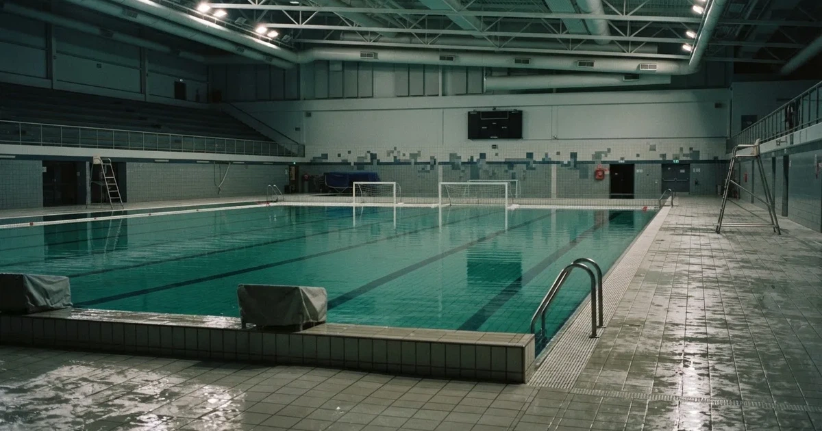 Ein Schwimmbecken mit türkisfarbenem Wasser und zwei schwimmenden Torrahmen am gegenüberliegenden Beckenrand, menschenleer unter Hallenlicht.