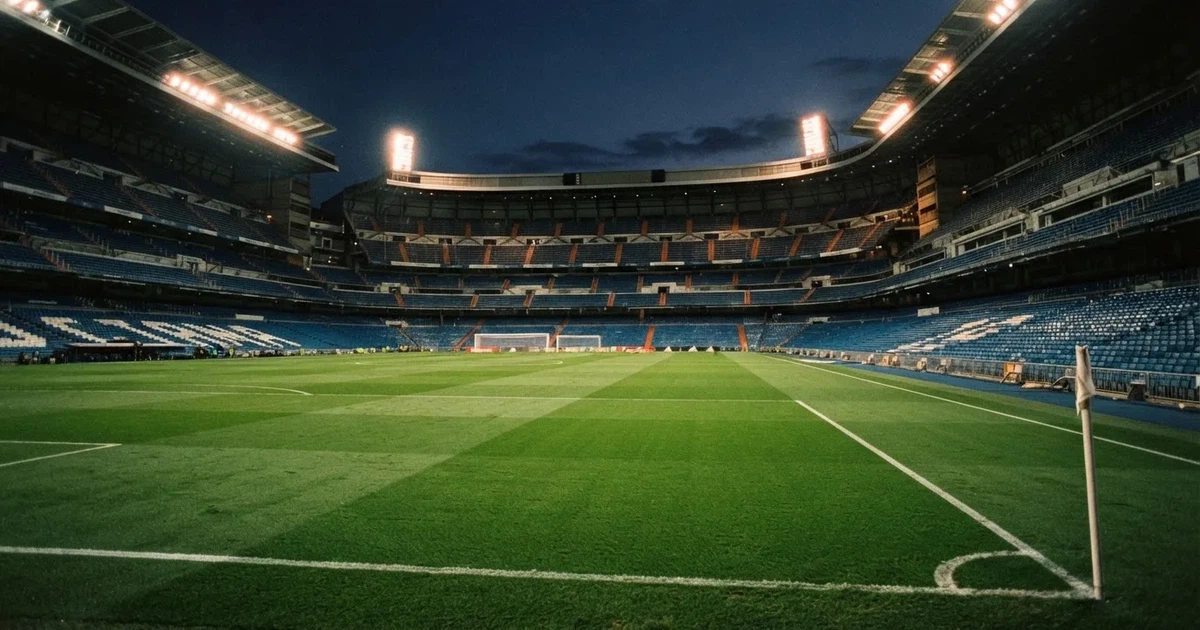 Ein Fußballstadion am Abend unter Flutlicht aus der Ferne gesehen, die Tribünen sind leicht beleuchtet und der Himmel dunkelblau.